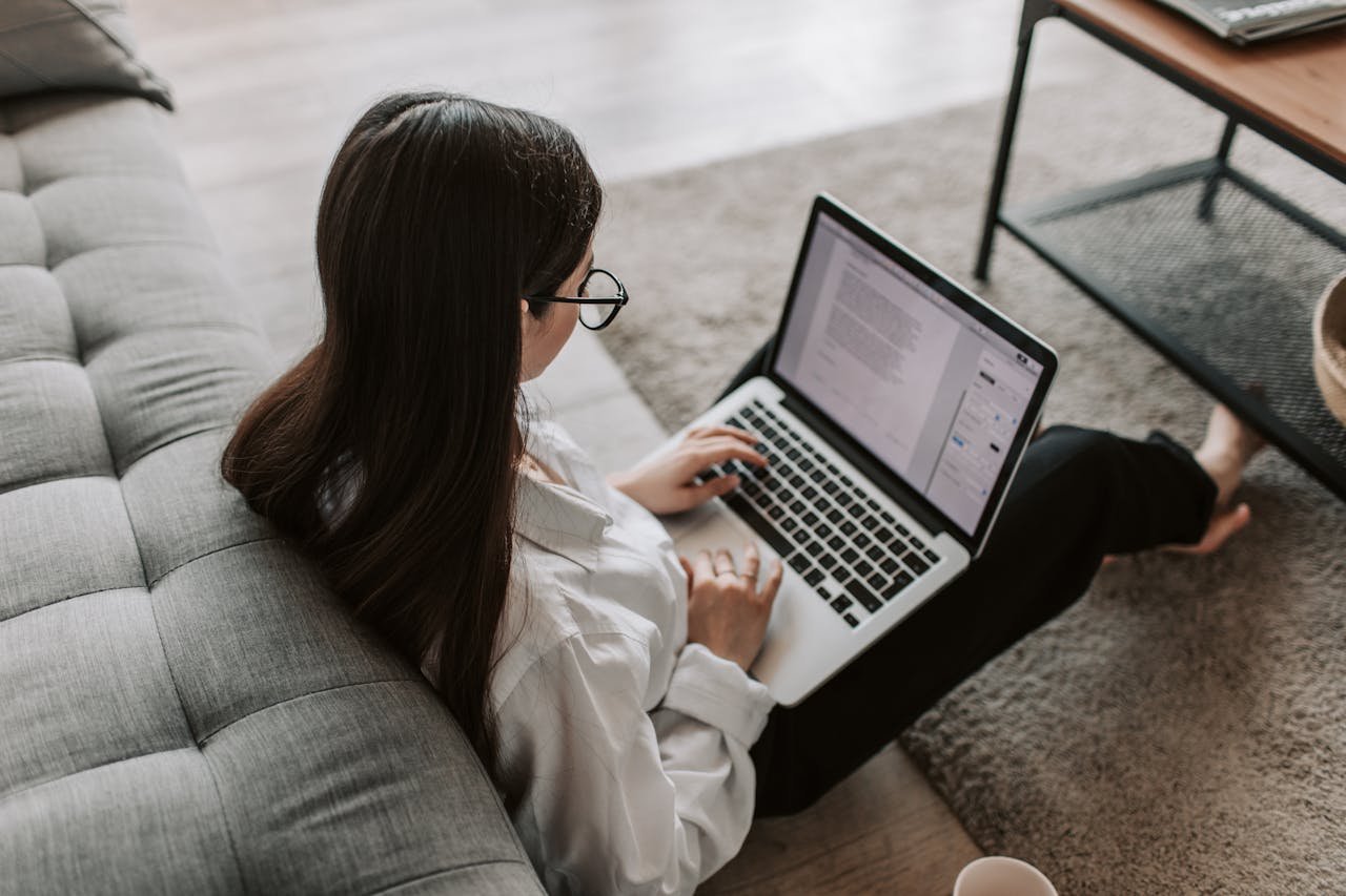 Services-02 Woman working remotely with a laptop on the floor next to a sofa, enjoying comfortable home office setup.