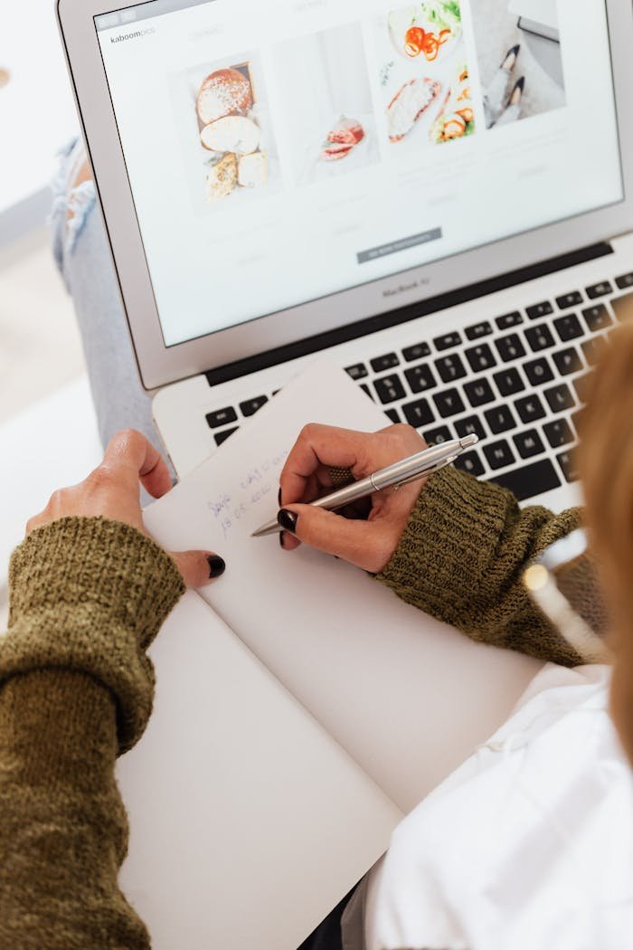digital Overhead view of a woman writing in a notebook while browsing on a laptop.